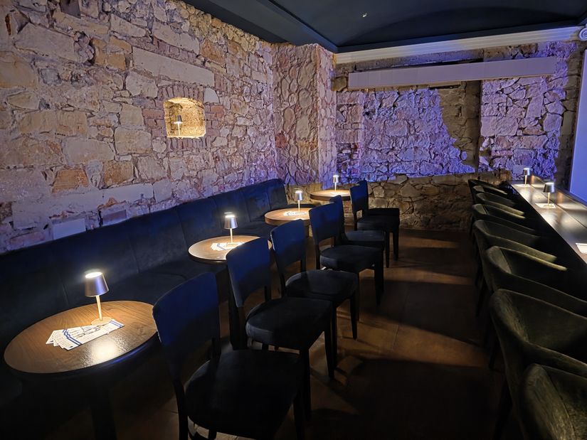 Seitlicher Blick auf die hinteren zwei Reihen mit Sitzgelegenheiten im Zuschauerraum; auf den Tischen kleine leuchtende Lampen