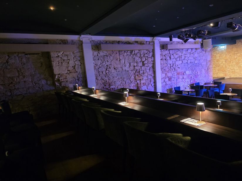 Schräger, seitlicher Blick auf die Sitzgelegenheiten im Zuschauerraum; auf den Tischen kleine leuchtende Lampen