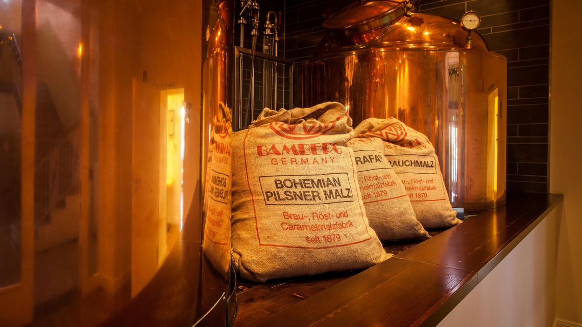 Zwei große Braukessel und drei Malz-Säcke davor